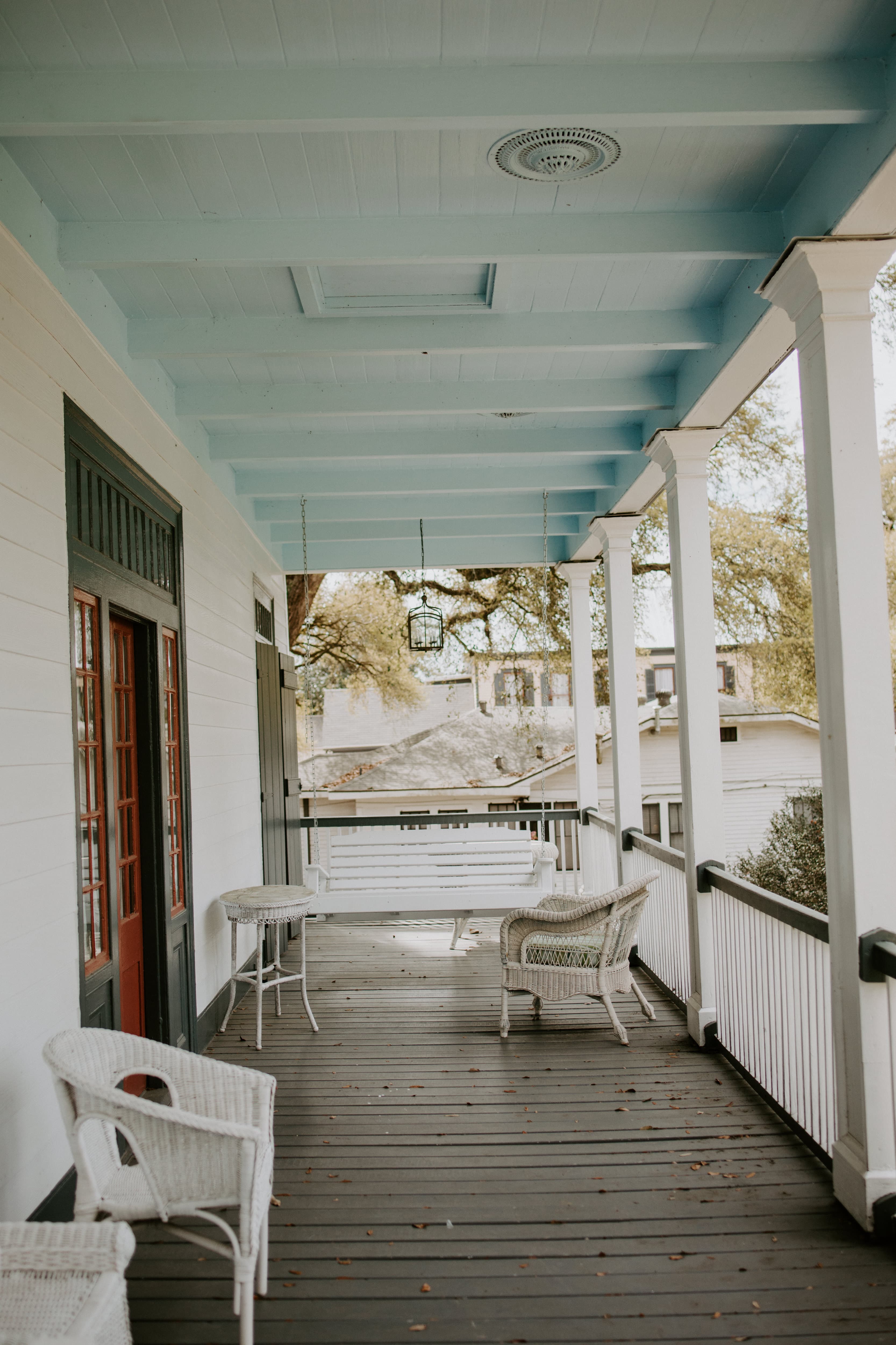 A serene porch featuring wicker furniture, a wooden floor, and a soft blue ceiling.