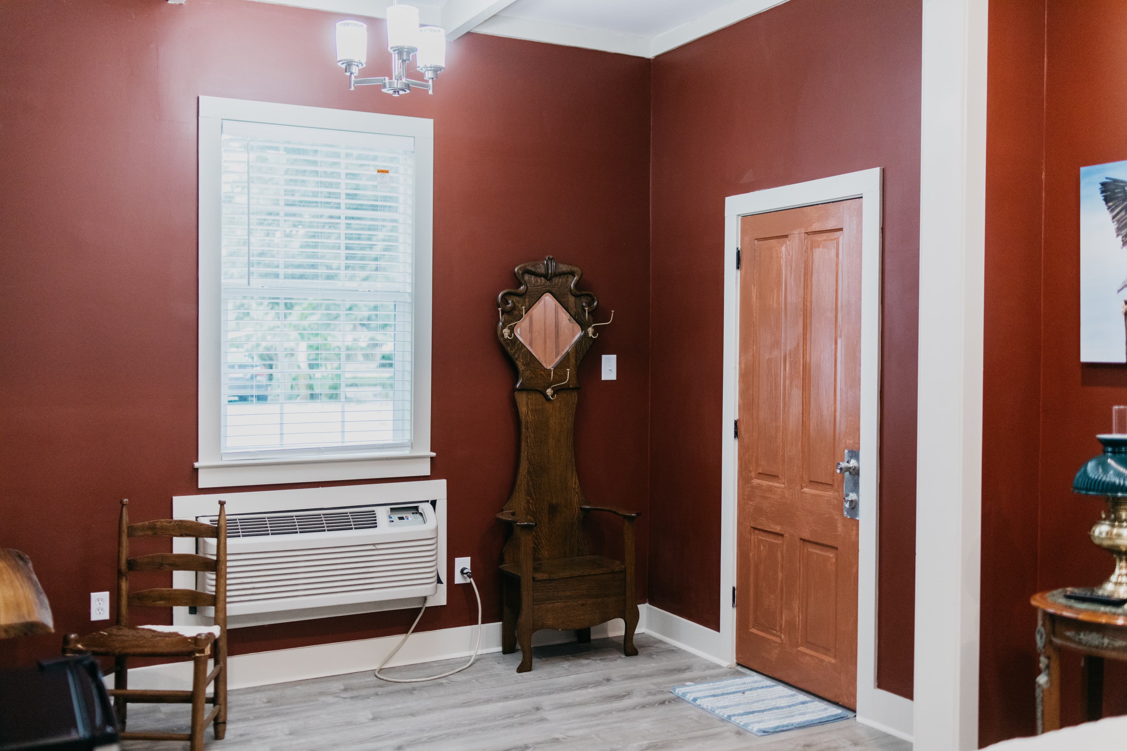 Interior of a room with red walls, featuring an ornate wooden chair, a window, and a door.
