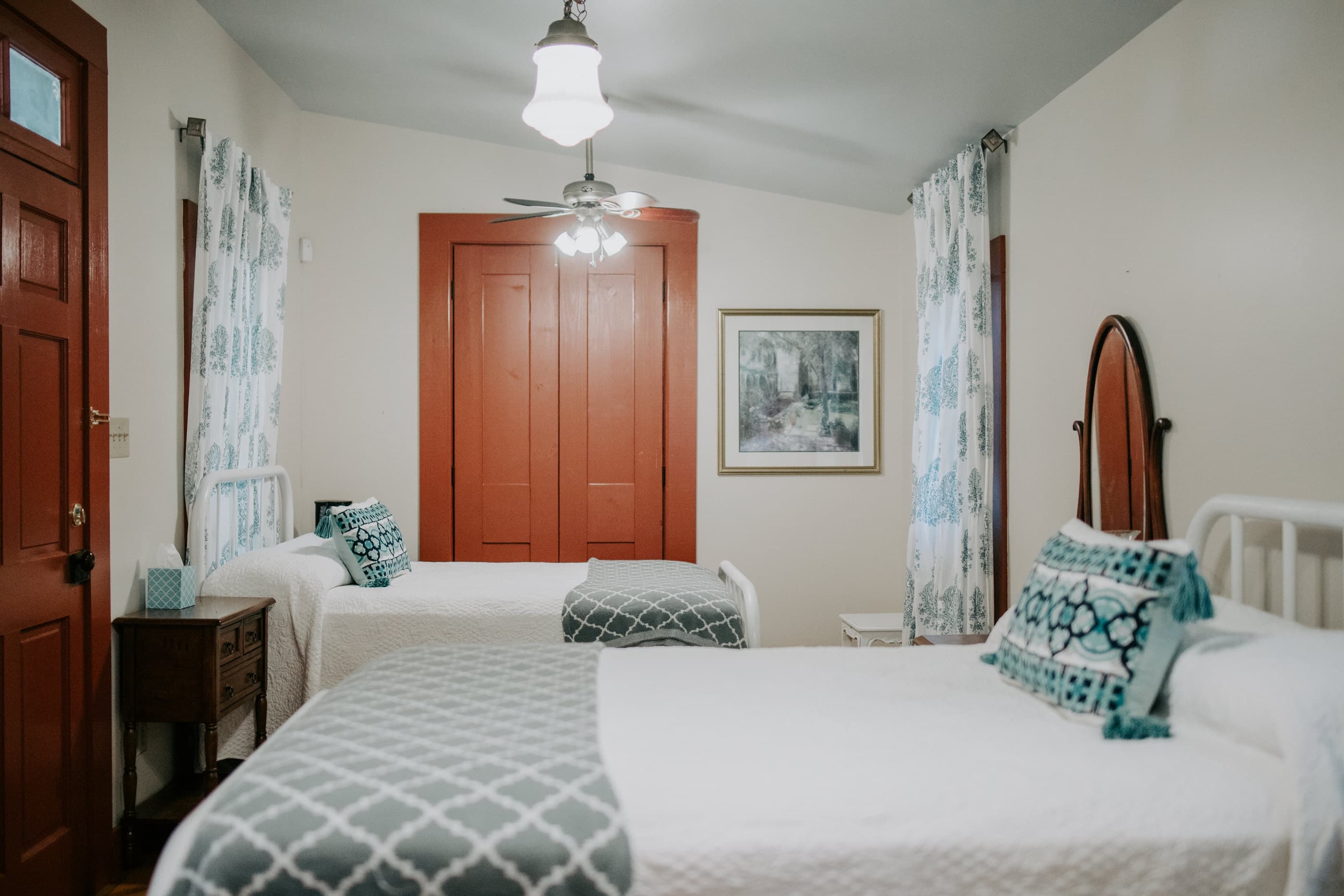 A cozy bedroom with two beds, colorful throw pillows, a ceiling fan, and a warm color scheme.